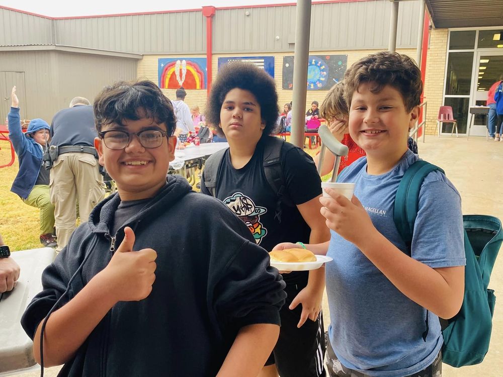 students giving a thumbs up while sitting a table holding plates