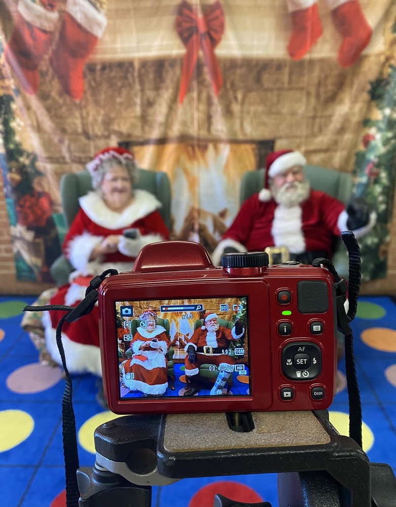 santa claus and mrs clause sitting in front of a fire decoration seen through the viewfinder of a camera