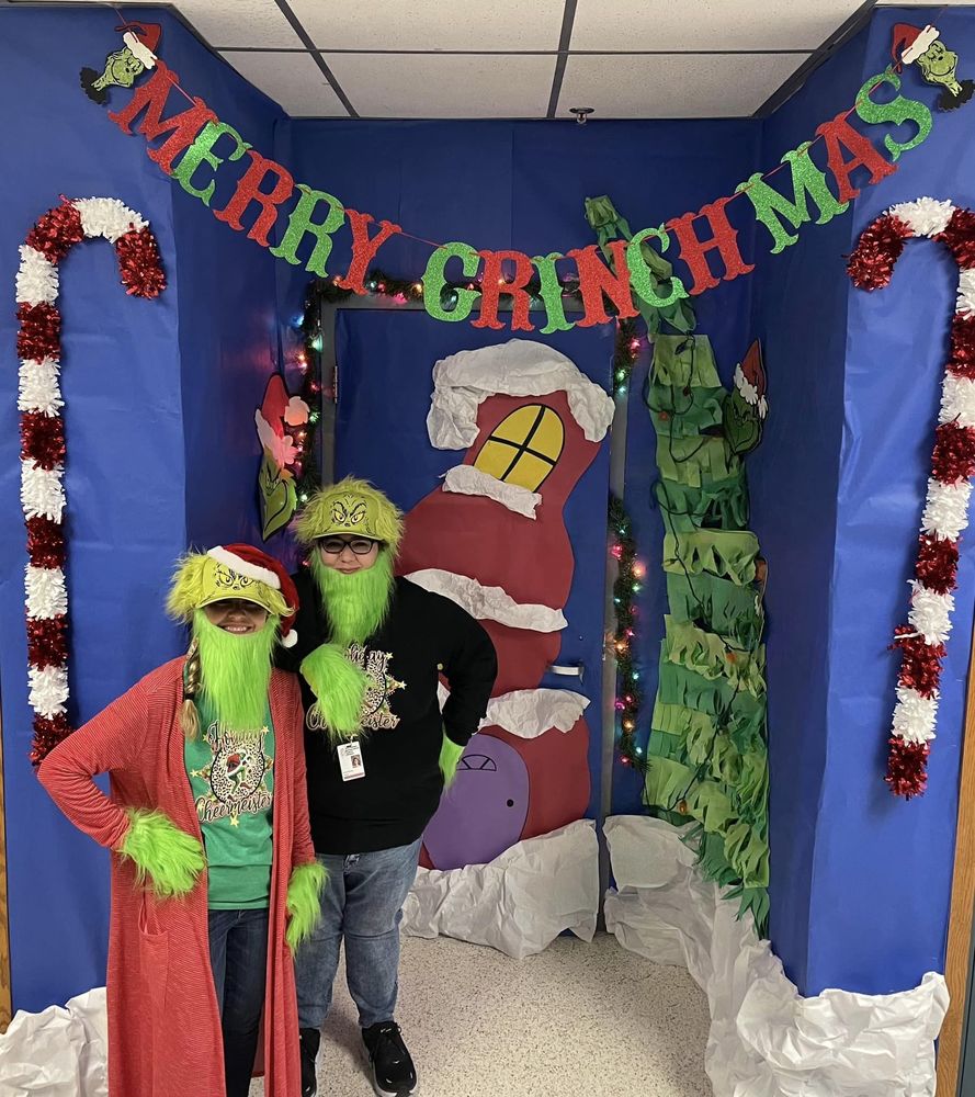 students standing in front of a merry christmas decorated wall in grinch costumes